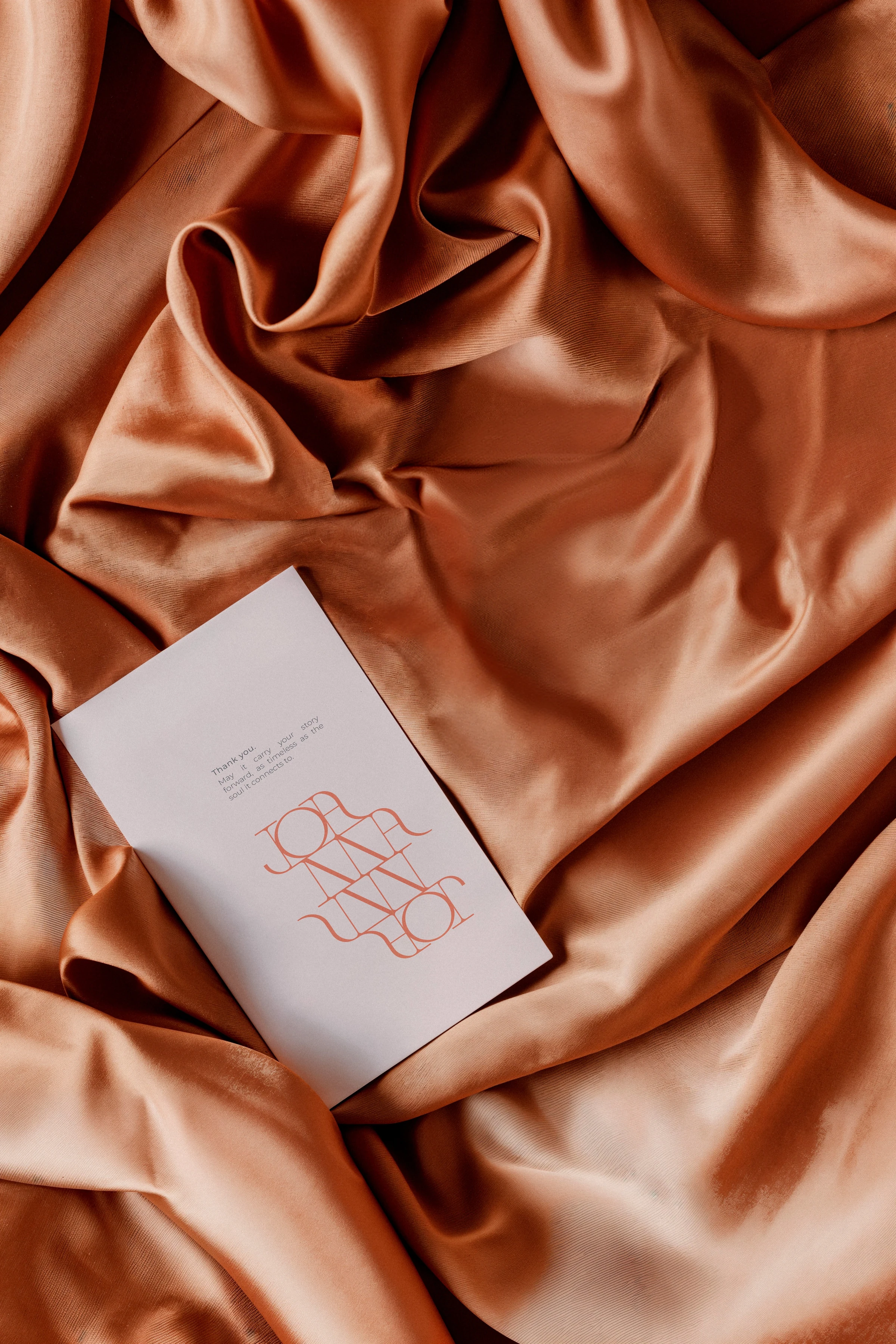 Joanna Achkar monogram card on copper-colored fabric