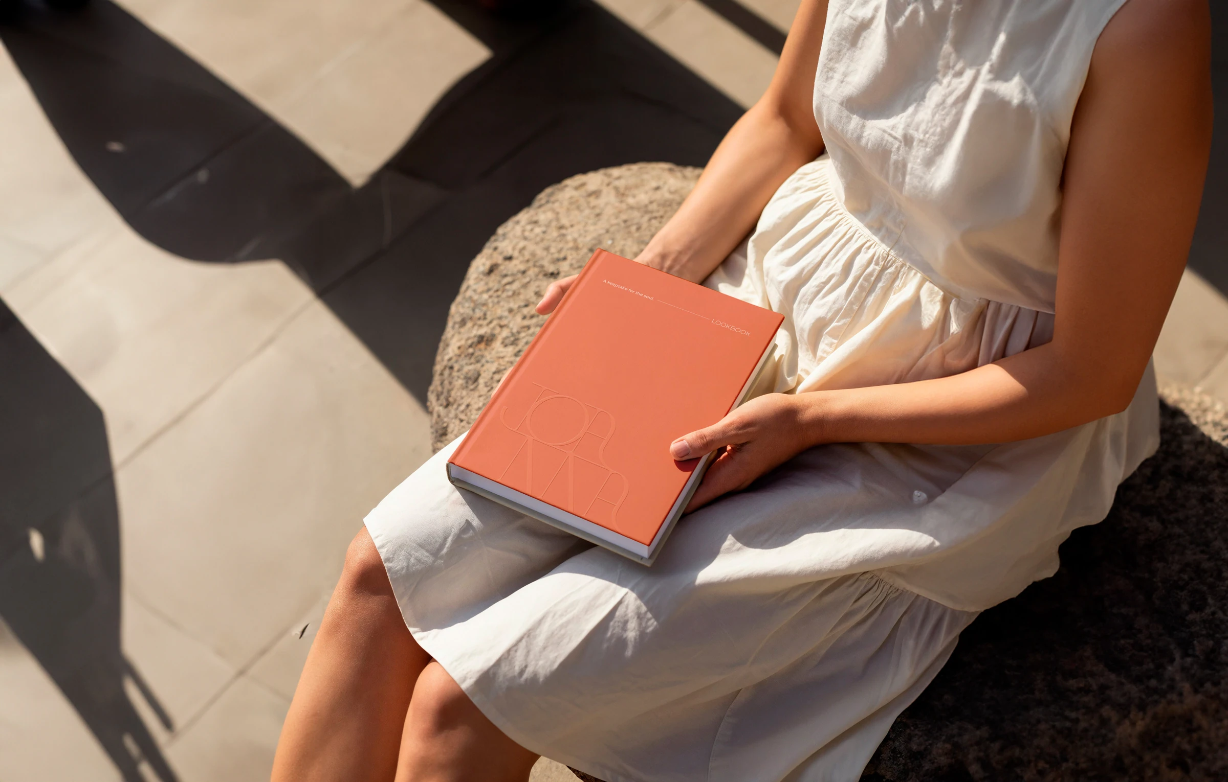Person holding a coral Joanna Achkar folder in sunlight